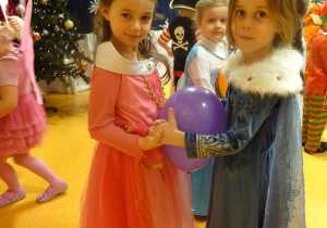 Dwie dziewczynki tańczą z balonem ułożonym pomiędzy brzuchami.